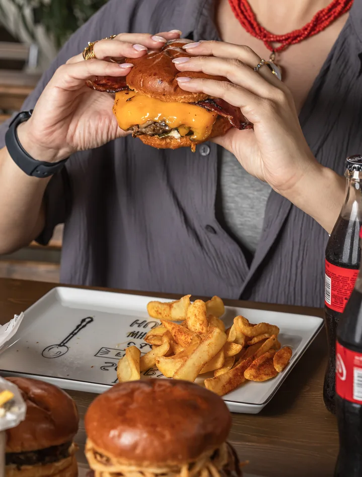 Guest holding a juicy Bee burger with both hands, fries on the table